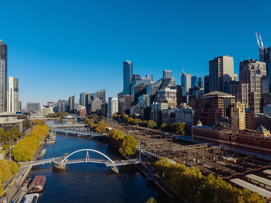 High-angle view of a bustling city of Melbourne skyline featuring modern skyscrapers and urban architecture under a clear blue sky during the day. Drone flight with CASA RPA licence